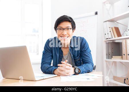 Porträt von fröhlich asiatischen Jungen Geschäftsmann arbeiten mit Laptop am Arbeitsplatz Stockfoto