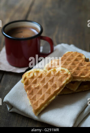 herzförmige Waffeln und Kaffee am Tisch in der Nähe von Stockfoto