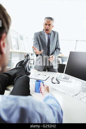 Entspannung am Schreibtisch, während sein Chef schreien wütend Geschäftsmann Stockfoto