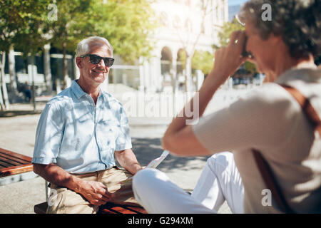 Hübscher senior Mann von seiner Frau fotografiert. Senior Tourist Fotos mit Kamera im Freien in der Stadt zu reden. Stockfoto