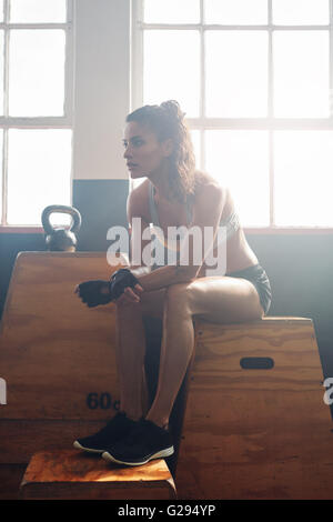 Muskulöse junge Frau sitzt auf einem Feld in Turnhalle nach ihrem Fitness-Training. Sportlerin, die Pause nach dem Training im Fitness-Studio. Stockfoto