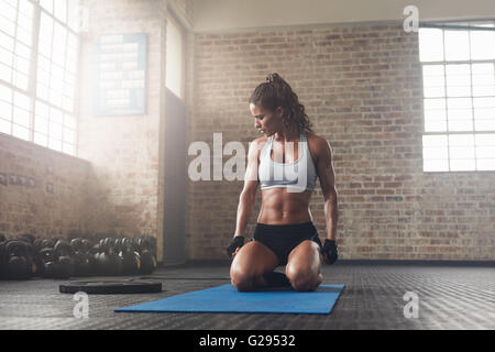 Innenaufnahme des Fitness junge Frau sitzt auf Yoga-Matte im Fitnessstudio. Muskulöse junge Sportlerin eine Pause von ihrem Training... Stockfoto