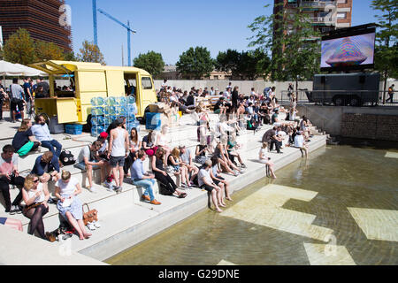 Die Teilnehmer sitzen draußen in der Sonne und beobachten die Vorträge vom Hauptsaal Roots Room auf einer großen Außenwand im OFFF Barcelona im Disseny Hub Museum of Design in Barcelona, Spanien, 26. Mai 2016. Der erste Tag des OFFF-Festivals (Let's Feed the Future) in Barcelona. Dieses Design-Festival ist jetzt sein 16. Jahr. Im Bild: Eine Menschenmenge versammelt sich draußen, um die Präsentationen auf einer Großleinwand anzusehen. Quelle: Rob Watkins/Alamy Live News Stockfoto