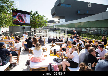 Die Teilnehmer sitzen draußen in der Sonne und beobachten die Vorträge vom Hauptsaal Roots Room auf einer großen Außenwand im OFFF Barcelona im Disseny Hub Museum of Design in Barcelona, Spanien, 26. Mai 2016. Der erste Tag des OFFF-Festivals (Let's Feed the Future) in Barcelona. Dieses Design-Festival ist jetzt sein 16. Jahr. Im Bild: Eine Menschenmenge versammelt sich draußen, um die Präsentationen auf einer Großleinwand anzusehen. Quelle: Rob Watkins/Alamy Live News Stockfoto