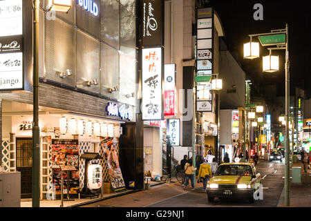 Kumamoto. Japanisches Restaurant, Diner, im Vordergrund mit Taxi, dann Aussicht auf schmalen City Centre Street, Leute. Nacht Zeit, Lichtwerbung. Stockfoto