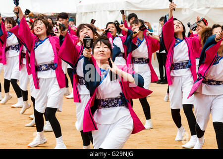 Japan, Kumamoto. Hinokuni Yosakoi Dance Festival. Frauen Mannschaft in Rosa happi Jacken, Tanzen und Holding naruko, hölzerne Klöppel. Im Freien, tagsüber. Stockfoto