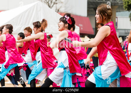 Japan, Kumamoto. Hinokuni Yosakoi Dance Festival. Frauen Mannschaft in Rosa happi Jacken, Tanzen und Holding naruko, hölzerne Klöppel. Im Freien, tagsüber. Stockfoto