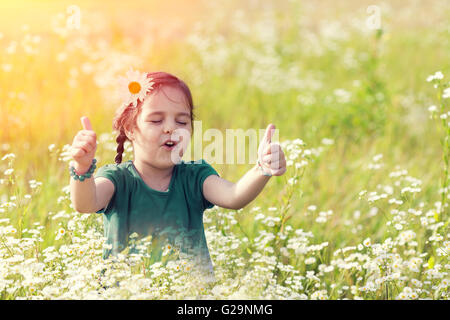 Glücklich singen kleine Mädchen mit dem Daumen nach oben auf der Blumenwiese Stockfoto