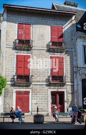 Menschen, die genießen eines sonnigen Tages vor einem typischen Gebäude von Saint-Jean-de-Luz. Aquitaine, Frankreich. Stockfoto