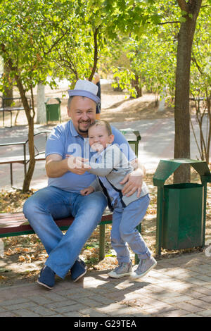 der Vater mit dem Sohn im Park auf einer Bank sitzen und Spaß haben Stockfoto