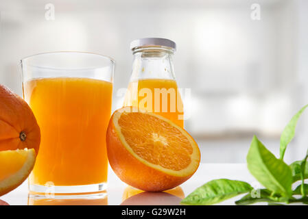 Gepresster Orangensaft in ein Glas auf einem weißen Küchentisch mit geschnittenen Orangen. Horizontale Komposition. Ansicht von vorne. Stockfoto