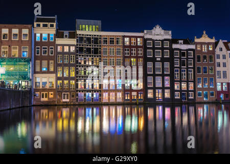 Schöne traditionelle alte Häuser in der Nacht in Amsterdam, Niederlande. Stadtbild mit reflektierten Stadtgebäude in Wasser mit blau Stockfoto