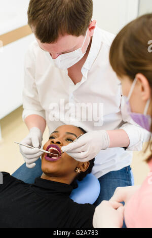 Schwarze amerikanische oder afrikanische Patientin mit Zahnarzt, Assistentin in einer zahnärztlichen Behandlung tragen Masken und Handschuhe Stockfoto