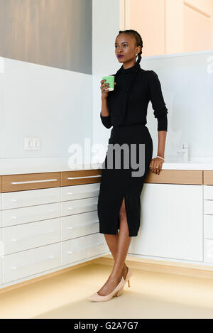 In voller Länge Portrait von eine Geschäftsfrau tragen schwarze und Beige Schuhe halten Einweg Tasse während der Arbeit an Licht Büro Stockfoto