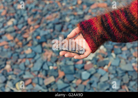 Eine Womans Hand hält ein Stück Schiefer außerhalb mit Kies und Geröll am Boden Stockfoto
