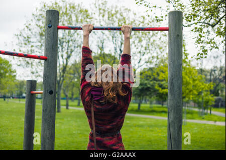 Eine junge Frau tut Pull ups in einem Park Stockfoto