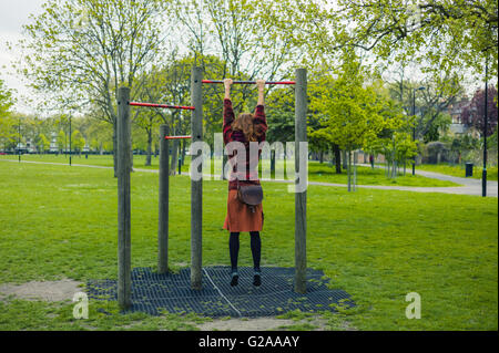 Eine junge Frau tut Pull ups in einem Park Stockfoto