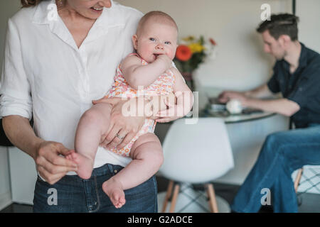 Mutter mit Kind (2 bis 5 Monate) und Vater arbeitet im Hintergrund Stockfoto