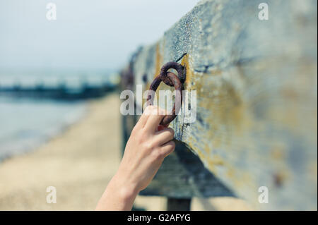 Eine junge weibliche Hand ist eine alte rostige Kette an einem Holzbalken befestigt greifen. Stockfoto