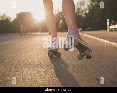 Die Beine einer jungen Frau wie sie Rollschuhlaufen in einem Park bei Sonnenuntergang Stockfoto