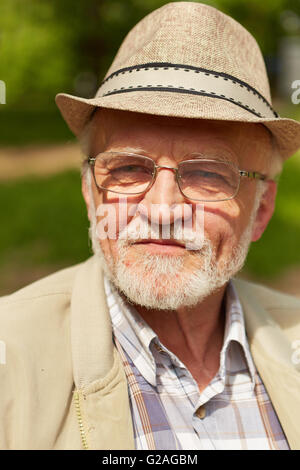 Nachdenklich Alter Mann mit Hut und Brille sitzt in einem Park im Herbst Stockfoto