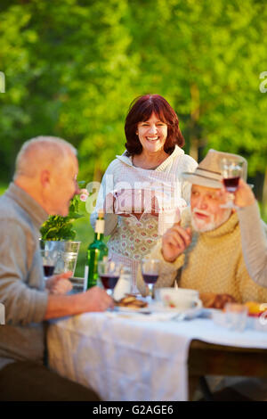 Glücklich Senioren Freunde feiert Geburtstag in einem Garten mit Kuchen und Rotwein Stockfoto