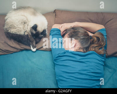 Eine junge Frau schläft in einem Bett mit einer Katze neben ihr Stockfoto