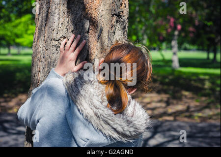 Eine junge Frau verbirgt sich hinter einem Baum im park Stockfoto