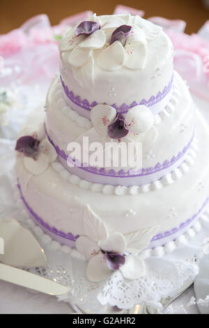 Weiße Hochzeitstorte mit Marzipan Orchideen und lila Spitze verziert Stockfoto