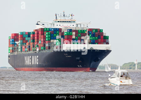 Extrem große Containerschiff Yang Ming Wert an der Elbe in der Nähe von Hamburg. Kleines Motorboot im Vordergrund. Stockfoto