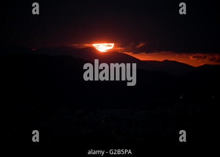 Sonnenuntergang über dem Egaleo Gebirge Athen Griechenland // ATHEN, Griechenland – Ein dramatischer roter Sonnenuntergang beleuchtet die westliche Skyline von Athen. Die Sonne untergeht hinter dem Egaleo-Gebirge, das die westliche Grenze der Stadt bildet und eine Höhe von 468 Metern (1.535 Fuß) erreicht. Die Silhouetten von Gebäuden im westlichen Athen und möglicherweise Teilen von Piräus, die etwa 12 km (7,5 Meilen) südwestlich von Zentral-Athen liegen, sind vor dem lebendigen Himmel sichtbar. Diese Szene, die in Athen aufgrund des mediterranen Klimas häufig ist, wird durch die atmosphärischen Bedingungen und die Höhe der Stadt von 70-300 Metern (230-984 fe Stockfoto