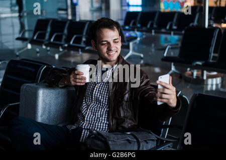 Porträt eines jungen Mannes Lachen und nehmen Selfie mit Kaffee am Flughafen warten, seinen Flug Stockfoto