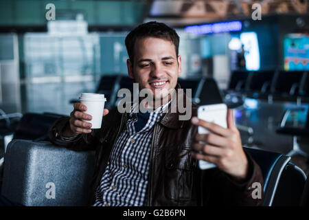 Porträt eines jungen Mannes Lachen und nehmen Selfie mit Kaffee am Flughafen warten, seinen Flug Stockfoto