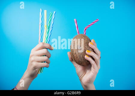 Womans Hand hält eine Kokosnuss und Strohhalme vor blauem Hintergrund Stockfoto