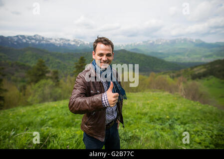 Junger Mann, Daumen hoch und stehen in den Bergen Stockfoto