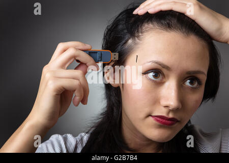 Close-up Schuss in den Kopf eine Business-Frau hält einen Memory-Stick, stecken Sie es in die Seite des Kopfes, erschossen auf einem grauen Hinterg Stockfoto