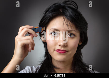 Close-up Schuss in den Kopf eine Business-Frau hält einen Memory-Stick, stecken Sie es in die Seite des Kopfes, erschossen auf einem grauen Hinterg Stockfoto