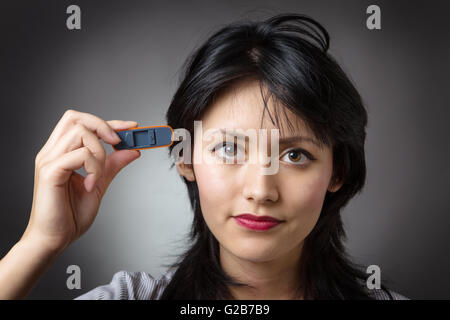 Close-up Schuss in den Kopf eine Business-Frau hält einen Memory-Stick, stecken Sie es in die Seite des Kopfes, erschossen auf einem grauen Hinterg Stockfoto