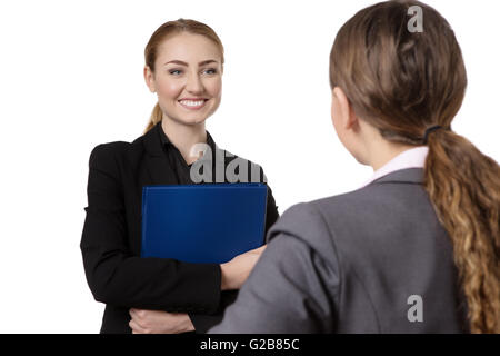 zwei Business-Frauen ein Gespräch.  Man hält einen blauen Ordner.   Schuss ist über eines der Womens Schulter getroffen. Stockfoto