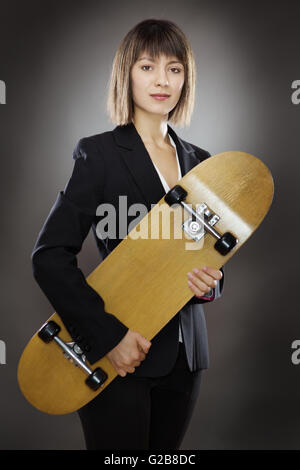 professionell aussehende Geschäftsfrau hält eine Skateboard gedreht im Studio auf einem grauen Hintergrund niedrig wichtige Beleuchtung Stockfoto