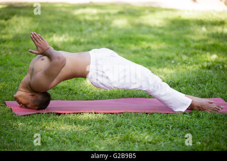 Attraktive indische junger Mann in weißem Leinen Kleidung praktizieren Yoga, Fitness, Pilates im Park, unterstützt Brücke auf dem Kopf zu tun Stockfoto