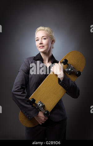 Studioaufnahme von einer Business-Frau mit einem hölzernen Skateboard hautnah.  Schuss auf grauem Hintergrund. Stockfoto