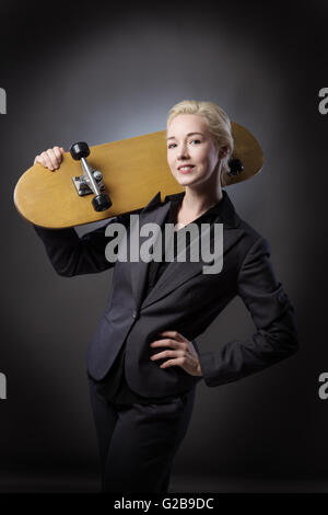 Studioaufnahme von einer Business-Frau mit einem hölzernen Skateboard hautnah.  Schuss auf grauem Hintergrund. Stockfoto