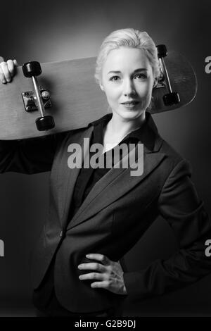 Studioaufnahme von einer Business-Frau mit einem hölzernen Skateboard hautnah.  Schuss auf grauem Hintergrund. Stockfoto