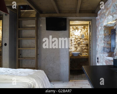 Tenaro blau Retreat in Mani, Griechenland. Teilweise Blick auf ein Schlafzimmer und Badezimmer Waschbecken durch eine offene Tür. Steinmauern und Leiter. Stockfoto