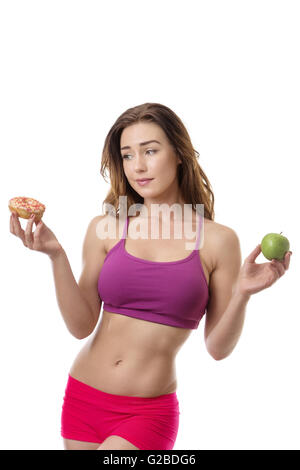 Schlank, Fitness Modell zu entscheiden, ob sie in ihrer linken Hand den Donut in ihrer rechten Hand oder der Apfel essen sollte Stockfoto