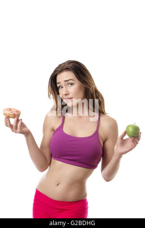 Schlank, Fitness Modell zu entscheiden, ob sie in ihrer linken Hand den Donut in ihrer rechten Hand oder der Apfel essen sollte Stockfoto