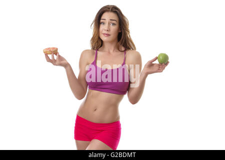 Schlank, Fitness Modell zu entscheiden, ob sie in ihrer linken Hand den Donut in ihrer rechten Hand oder der Apfel essen sollte Stockfoto