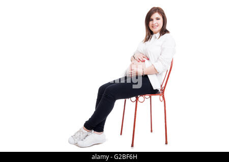 Schöne schwangere Frau sitzen auf Stuhl und streichelte ihren Bauch und suchen glücklich auf weißen Studio-Hintergrund mit Exemplar Stockfoto