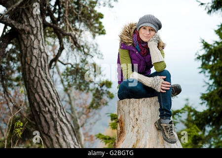 Frau Winter Kleidung sitzt auf einem Baumstumpf Stockfoto